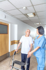 Asian nurse helping elderly man with walker in hospital aisle