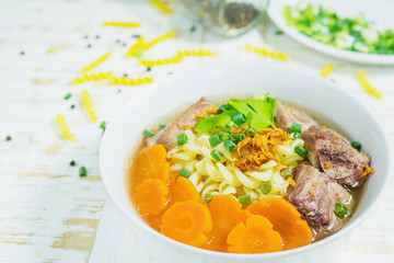 Macaroni soup with pork and carrot on white wooden table - delicious and healthy food concept
