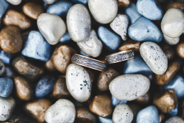 Two black and gold wedding rings on stone painted multicolor background
