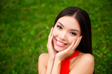 Close up portrait of dreamy and charming dark-haired young woman who looks into the camera touching her palms up to the face