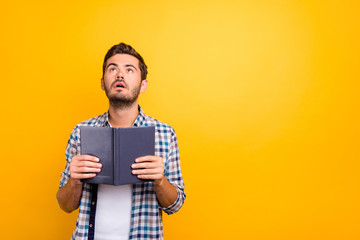 Portrait of thoughtful man holding book looking up isolated on shine yellow background with copy space for text
