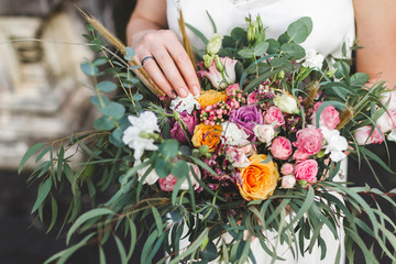 Bride holding in hands beautiful bouquet of flowers in boho style with yellow and pink roses and green bunches © Oleg Breslavtsev