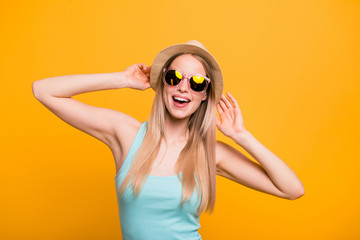 Attractive nice cute straight-haired blonde caucasian smiling girl, wearing casual blue shirt, cap, sun glasses. Enjoying vacation. Isolated over yellow background