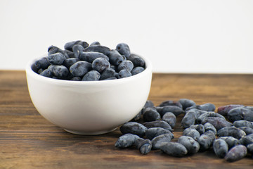 Fresh ripe honeysuckle berries in a ceramic bowl on a wooden board. Healthy breakfast. White bowl of honeysuckle.