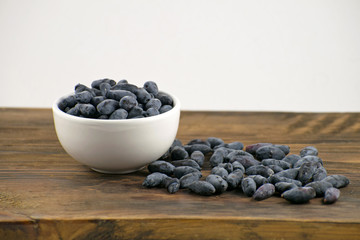 Fresh ripe honeysuckle berries in a ceramic bowl on a wooden board. Healthy breakfast. White bowl of honeysuckle.