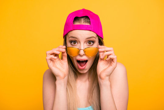 Summer discounts for travel! Close up portrait of shocked and surprised girl looks at the camera over glasses with wide-open eyes and mouth isolated on shine yellow background.