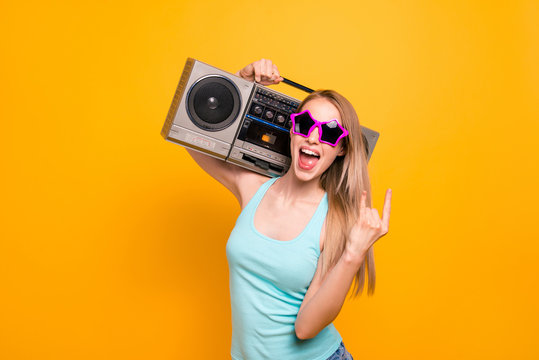Stylish and young fashion blonde giving the Rock and Roll sign and holds a tape recorder on her shoulder isolated on vivid yellow background