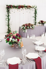 Wedding table, decorated with red flowers bouquets, candles, grey tablecloth, and white plates
