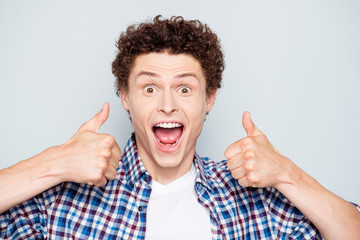 Portrait of young laughing guy showing double thumbs up gesture. Isolated over grey background