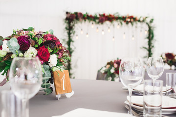 Wedding table, decorated with red flowers bouquets, candles, grey tablecloth, and white plates