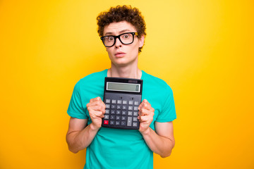 Attractive curly-haired young guy student, wearing casual green t-shirt, showing zero on calculator. Isolated over vivid bright yellow background