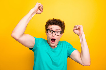 Handsome curly-haired shocked young guy wearing casual green t-shirt and glasses, showing surprised...