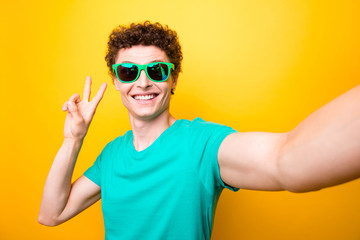 Self portrait of handsome curly-haired glad young guy wearing casual green t-shirt and colorful sun...