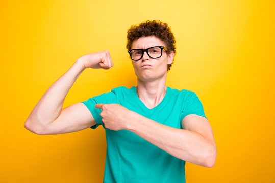 Handsome curly-haired young guy wearing casual green t-shirt and glasses, showing muscles. Isolated over yellow background