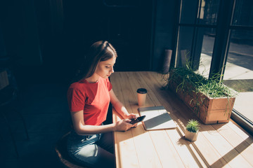 Attractive nice serious young girl freelancer student wearing casual sitting in cafeteria typing email in smartphone, dark interior