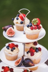 Fresh tasty cupcakes with berries on wedding reception table, decorated in red colour with flowers