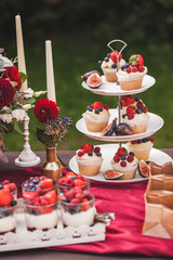 Fresh tasty cupcakes with berries on wedding reception table, decorated in red colour with flowers