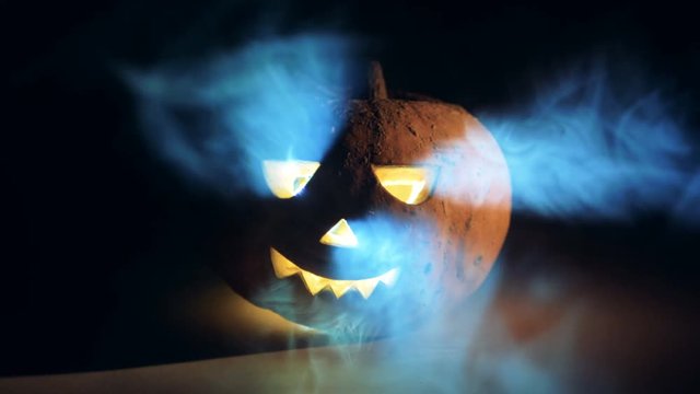 Clouds of smoke are wreathing around a halloween pumpkin. Scary carved halloween pumpkin