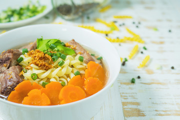 Macaroni soup with pork and carrot on white wooden table - delicious and healthy food concept