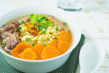 Macaroni soup with pork and carrot on white wooden table - delicious and healthy food concept