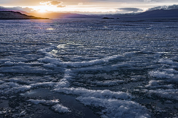 picturesque view of frozen wild lake under orange sky at sunset 

