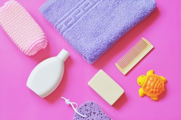 Flat lay baby bath products/ Purple sponge, shampoo, rubber turtle toy, soap bar and wooden comb on a pink background