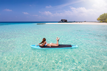 Fernweh Konzept: attraktive Frau im Bikini sonnt sich auf einem Sufbrett über den tropischen...
