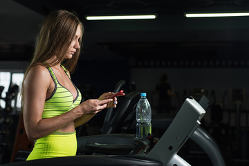 Fototapeta na wymiar Caucasian girl running on a treadmill holding her mobile phone in the gym
