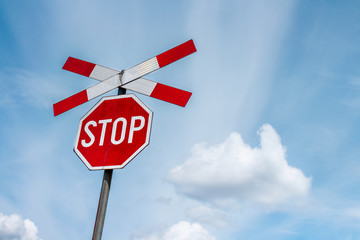 Red stop sign with railway cross sign and blue sky with white clouds in background