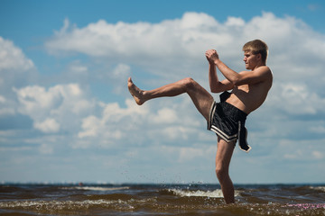 Kickboxer kicks in the open air in summer against the sea.