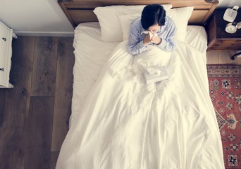 Sick woman on the bed blowing her nose - obrazy, fototapety, plakaty