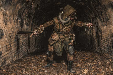 Post apocalyptic mutant creature or survivor in tatters and gas mask jumps out of darkness and...