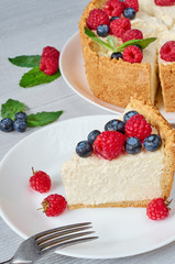A piece of classic New York cheesecake with fresh raspberries, blueberries and mint leaves on the white plate on the gray kitchen background. Close up view
