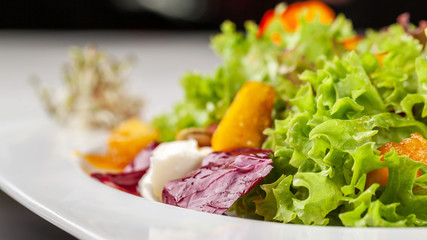 European Italian salad of lettuce, cherry tomatoes, pumpkin, edible pumpkin flowers, and pumpkin seeds, in a white plate. Copy space, selective focus
