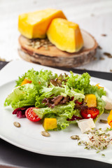 European Italian salad of lettuce, cherry tomatoes, pumpkin, edible pumpkin flowers, and pumpkin seeds, in a white plate. Copy space, selective focus