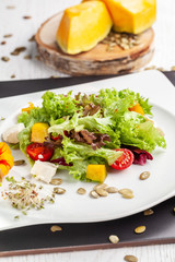 European Italian salad of lettuce, cherry tomatoes, pumpkin, edible pumpkin flowers, and pumpkin seeds, in a white plate. Copy space, selective focus
