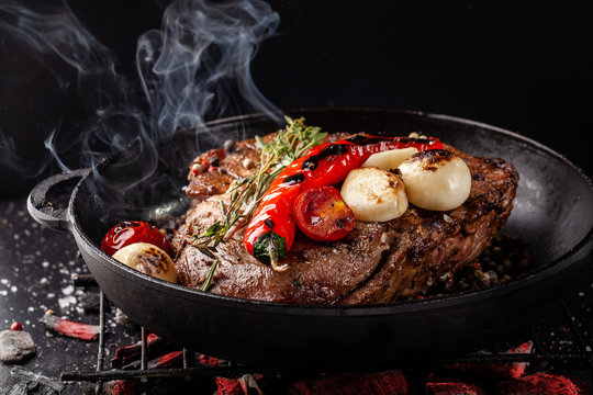 concept of the process of cooking meat. The steak is roasted on charcoal in a cast-iron frying pan, with spices, garlic, hot red pepper, squarish, thyme. image background. Copy space, selective focus