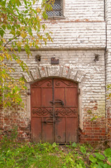 Old brown ornate metal double door in white brick wall. Gorodets, Nizhegorodsky region, Russia. 
