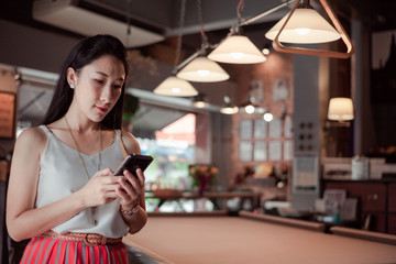 Beautiful Asian women Using smart Phone Emotional happiness on Pool Table in cafe restaurant or coffee shop .Post to Social Network and Social Media Online Internet On table in holiday.