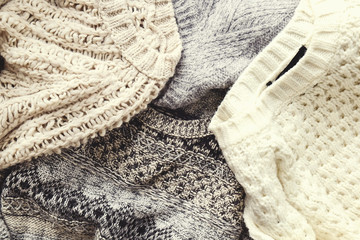 Bunch of knitted warm pastel color sweaters with different knitting patterns laid in messy pile, clearly visible texture. Stylish fall / winter season knitwear clothing. Close up, copy space for text.