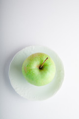 Green apple on white plate and white background. Overhead shot. Copy space