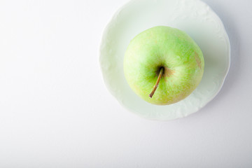 Green apple on white plate and white background. Overhead shot. Copy space