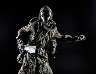 Low key portrait of post apocalyptic creature, living in catacombs mutant, survived in nuclear disaster human in ragged cloth and gas mask, armed with handmade cold weapon isolated on black background