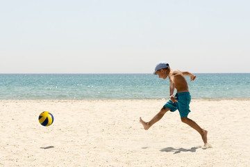 A boy playing football at the empty beach