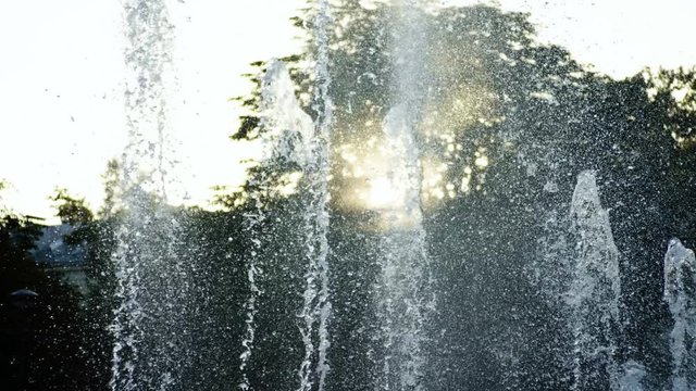 Close-up shot of water drops of fountain in summer park at sunset. 4K