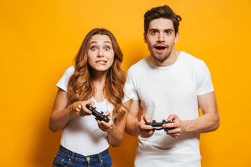 Image of excited young man and woman playing together and competing in video games using joysticks,...