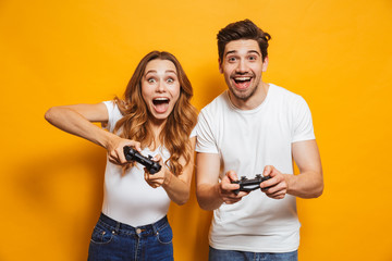 Photo of caucasian couple man and woman playing together video games using joysticks, isolated over...