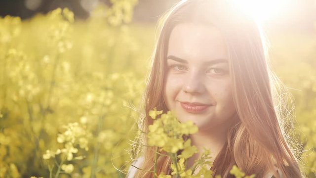 Portrait pretty girl looking into the camera in the rape field. Young woman walks in the rape's field, posing, and smiling at camera