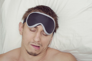 Man resting in a mask for sleep. Stubble on his face. Tired man