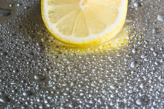 Slice of lemon on a steel reflective background with water drops close-up